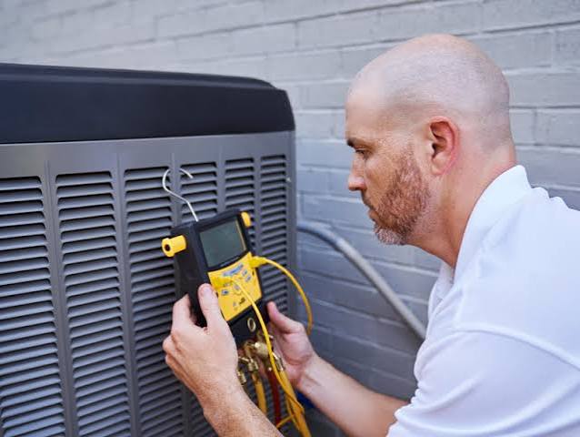 HVAC technician checking an outdoor condenser with diagnostic equipment