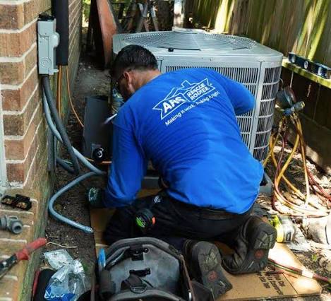 HVAC technician servicing an outdoor residential condenser in a narrow side yard